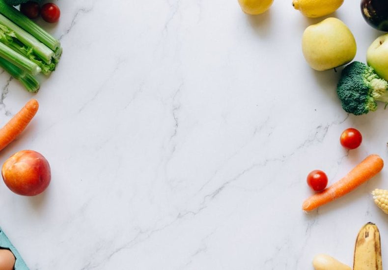 An assortment of fresh fruits and vegetables on a marble background, perfect for healthy lifestyle concepts.